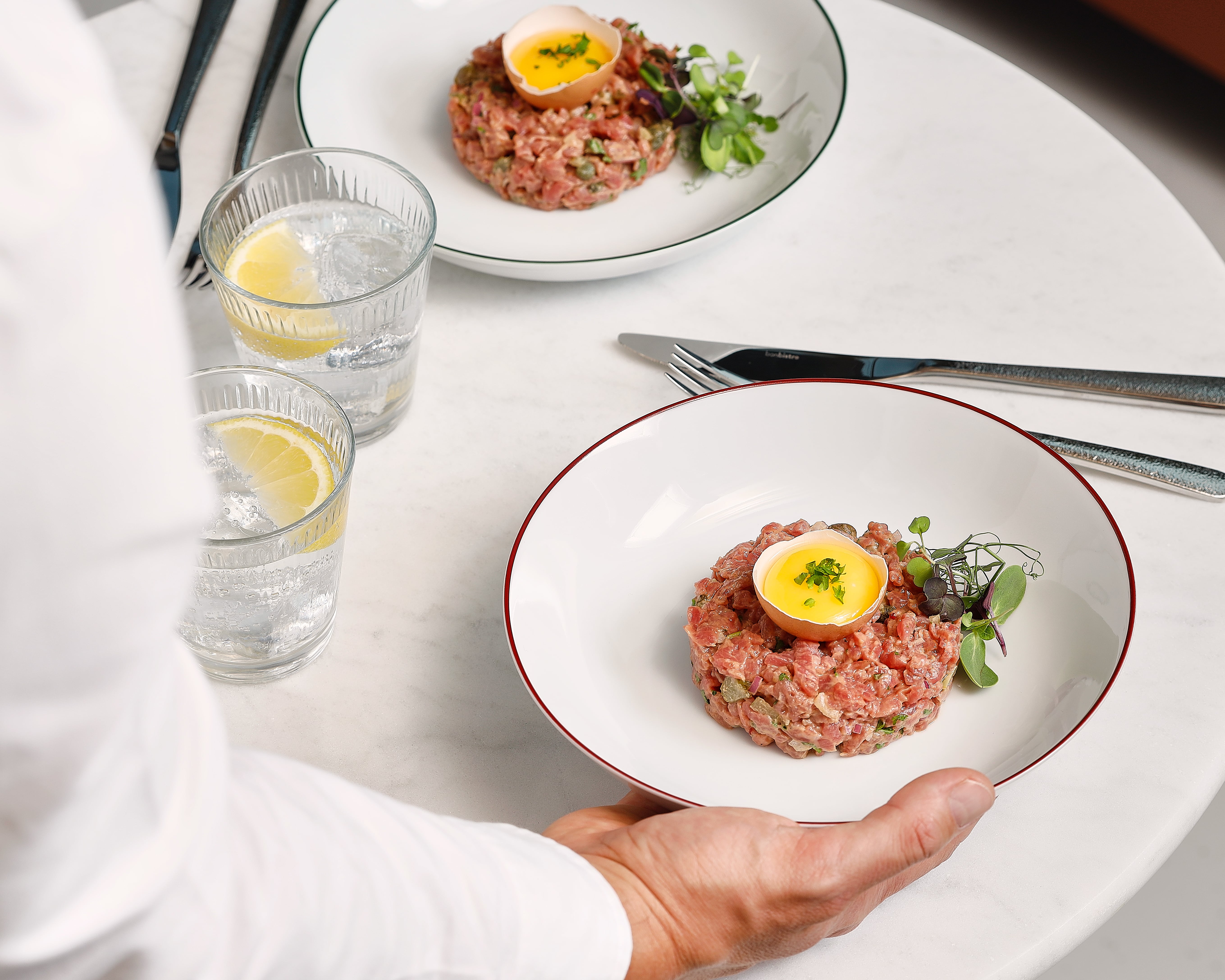 Basic White plates of refined steak tartare presented in a modern setting.